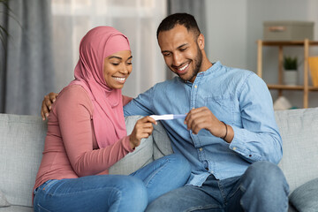 Obraz na płótnie Canvas Parenthood Concept. Happy Black Muslim Spouses Holding Positive Pregnancy Test At Home
