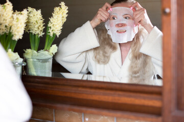 a middle-aged woman is busy with morning hygiene, she makes the face mask 