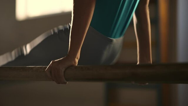 A young athlete performs a gymnastic exercise on the wooden parallel bars in the gym. Close-up