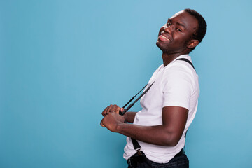 Fototapeta premium Handsome african ethnicity male model posing for camera while standing on blue background. Confident smiling heartily young man with vintage and attractive look. Studio shot