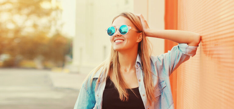 Summer portrait of beautiful blonde smiling young woman wearing sunglasses in the city