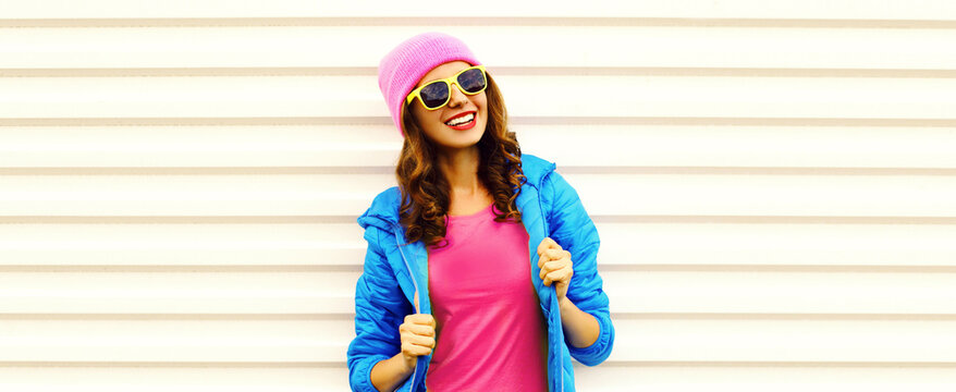 Portrait of stylish happy smiling young woman wearing colorful pink hat, blue jacket on white background