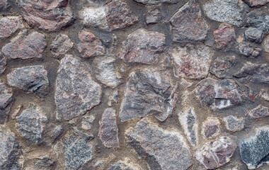 Natural stone wall background texture, showing a clearly brick-built natural stone wall with different size stones in brown and gray color. The stone wall constructed by gray wall