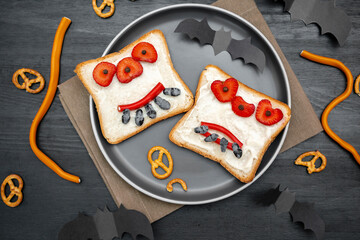 Funny monster face on halloween sandwich toast bread with butter, strawberry, sweets,cutting serving board,bats on black background close up. Kids child sweet dessert breakfast lunch food