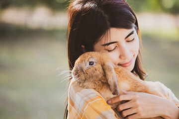 beautiful pretty portrait of young Asian woman person with cute rabbit in pet and animal care concept, happy female holding bunny at nature outdoor field with friendship, easter concept