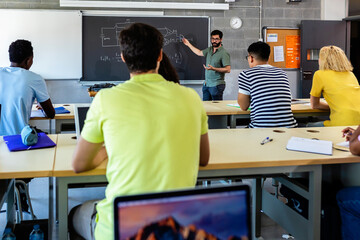 Young adult male lecturer teaching during technology class. Multiracial young students listening...