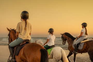 young woman with braid riding a horse on the beach next to 2 young riders