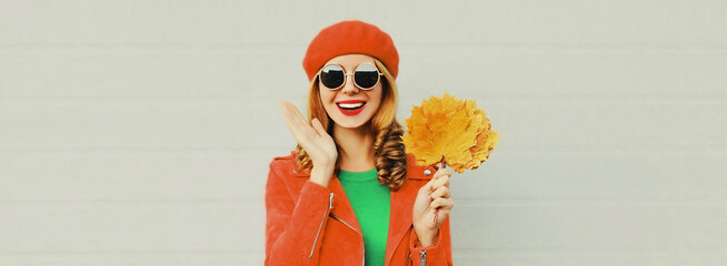 Autumn portrait of happy smiling young woman with yellow maple leaves wearing red french beret on gray background