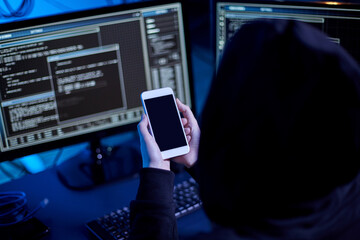 cybercrime, hacking and technology concept - close up of male hacker with smartphone using computer virus program for cyber attack in dark room