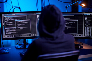 cybercrime, hacking and technology concept - hacker in dark room writing code or using computer...