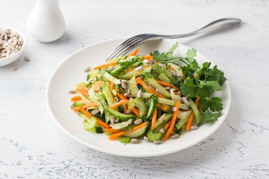 A plate with a salad of cucumbers, carrots, celery, seeds and parsley on a light blue background. Delicious healthy homemade food