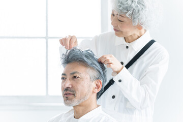 美容院で働く美容師とヘアセットされるシニア男性（美容・仕事）