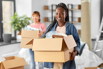 Fototapeta na wymiar moving, people and real estate concept - happy smiling women with boxes at new home