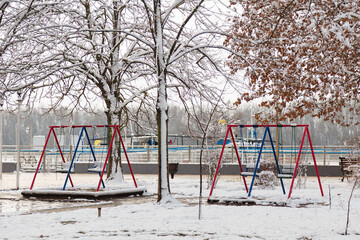 empty playground, bright swing set for children covered with snow on winter background, no people. Cold frosty weather, abandoned city - Powered by Adobe