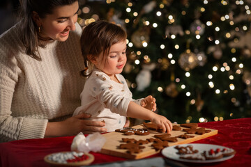 family, cooking and winter holidays concept - happy mother and baby daughter with icing in baking...
