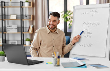 distant education, school and remote job concept - happy smiling male math teacher with laptop...