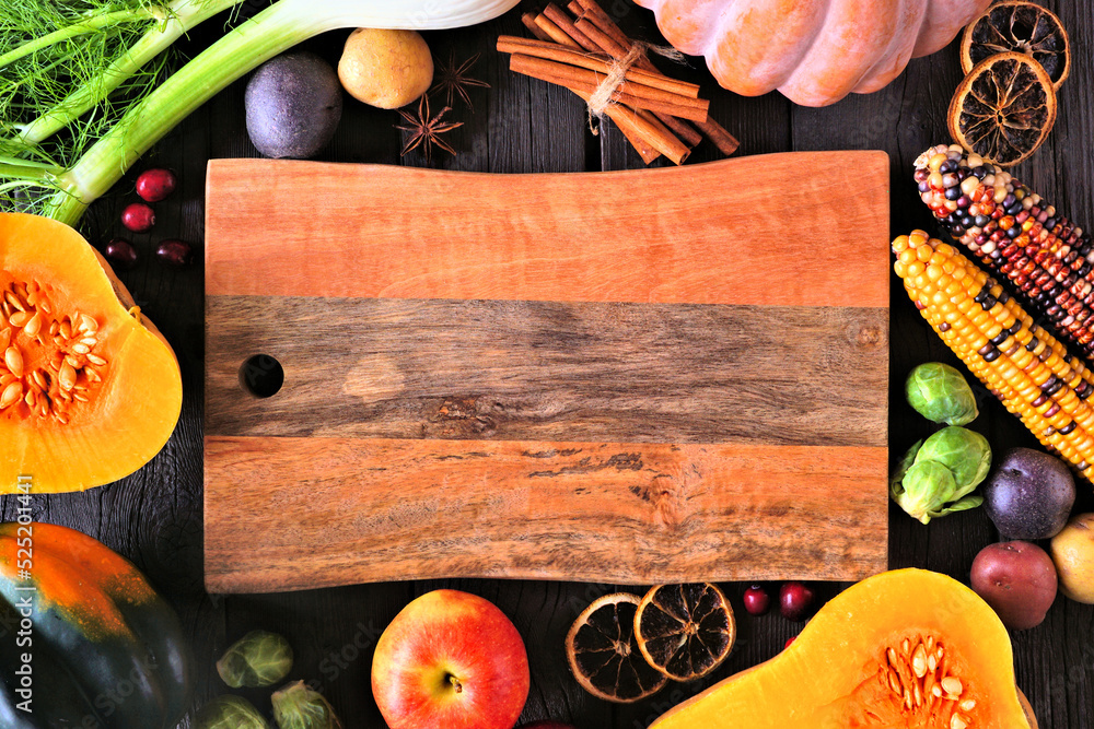 Wall mural Fall food frame of pumpkins, apples, squash and assorted vegetables surrounding a blank wood serving board. Top view on a dark wood background with copy space. - Wall murals