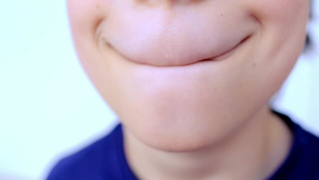 close-up and front view of mouth of caucasian child, boy of 10 years old in blue shirt makes funny faces, concept of sensory feelings, speech disorders, methods of correctional developmental exercises
