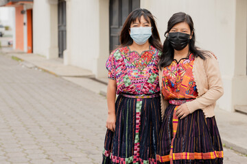 Hispanic young women with face mask on the street- happy Hispanic sisters in the village in Latin...