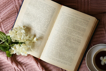 Beautiful jasmine flowers, open book and cup aromatic tea on pink fabric, flat lay