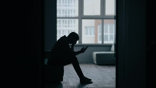 Stressed caucasian middle-aged man sitting on the sofa in bedroom while get bad news from mobile phone. Depressed and hopeless male being alone with negative emotion.