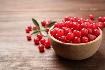 Tasty ripe cranberries on brown wooden table, closeup. Space for text