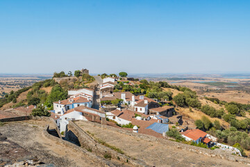 Cobblestone path of castle walls with street and houses of Monsaraz village on hill with Aqueva on the horizon, Alentejo PORTUGAL