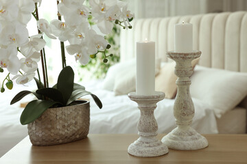 Pair of beautiful candlesticks and orchid plant on wooden table in bedroom