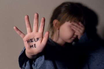 Crying little girl showing palm with phrase HELP ME near beige wall, focus on hand. Domestic...