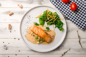 Salmon steak on the grill with spinach on white plate on white wooden table top view