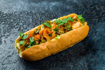 hot dog with shrimps and vegetables on dark stone table