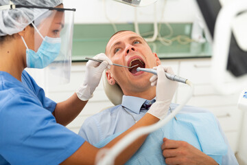 Practitioner female dentist drilling tooth to male patient businessman in dental studio