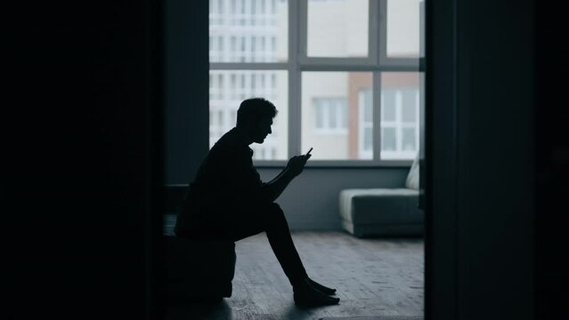 Silhouette man sitting on the sofa while get bad news from mobile phone. Depressed and hopeless male being alone with negative emotion. Mental health and economic life problem concept