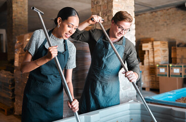 Cellar workers, making wine and mixing open tank with stirring, pressing and crushing tool for alcohol production. Happy staff and merchants in factory distillery, winery and manufacturing warehouse