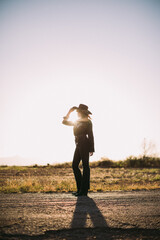 Woman in cowboy hat and western outfit standing full length with sun flare and desert landscape