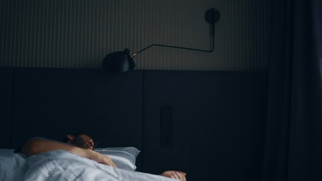 A bearded Caucasian middle-aged man wakes up in bed with neck and back pain. Not getting enough sleep and not sleeping well.