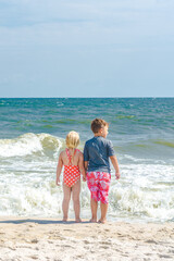Brother and sister hold hands with each other and starring on the ocean