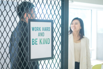 A sign in an office, Work hard and be kind. Office business people in the background.