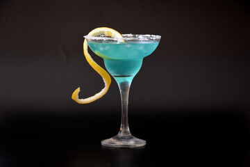A tall glass of Blue Curacao liqueur with lemon zest and sugar rimmed on a black background.