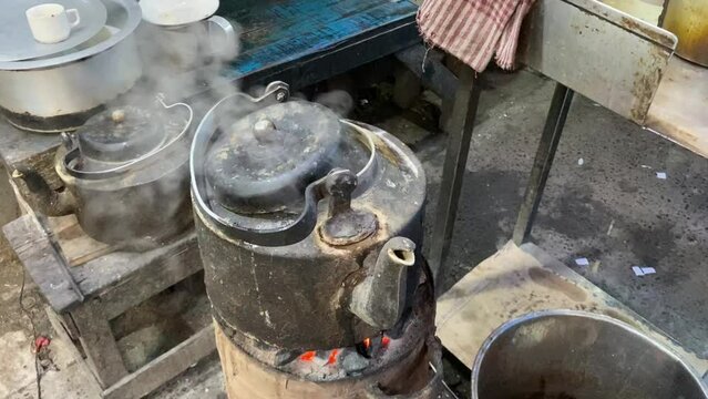 Boiling tea on clay stove with an old black cast iron kettle, traditional cooking methods used in countryside using firewood and fire flames in Kolkata, India