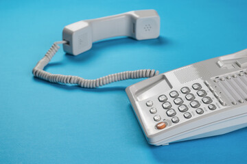 A light office phone with the handset off on a blue background.