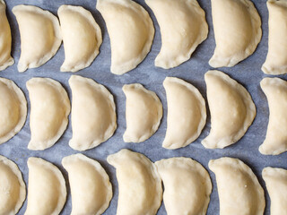 Homemade vareniki or dumplings, filled with cottage cheese or mashed potato on baking sheet. Cooking raw dumplings with potatoes. Top view, rural style. Ukrainian and russian national dish.
