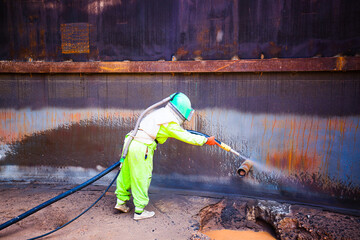 .sandblasting process Sandblasting industrial workers prepare to clean steel surfaces of oil drums before painting in the factory.