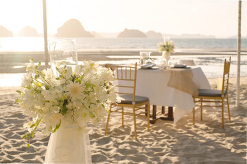Beautiful table set up for a romantic dinner on the beach with  flowers and candles. Catering for a romantic date, wedding or honeymoon background. Sunset beach dinner. selected focus.