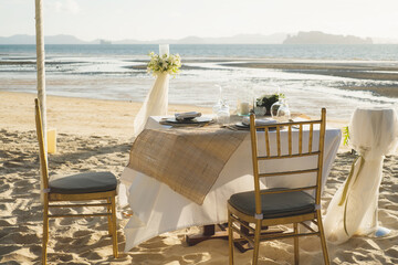 Beautiful table set up for a romantic dinner on the beach with  flowers and candles. Catering for a romantic date, wedding or honeymoon background. Sunset beach dinner. selected focus.