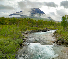 A partially misty mountain with a cold, fiercely flowing, meltwater stream beneath it in Swedish Lapland.  - 525228615