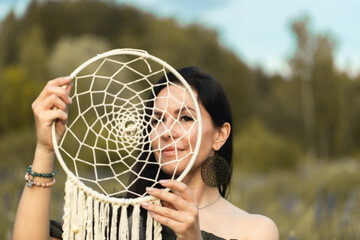 An attractive woman in a summer field with a dream catcher. Front view.