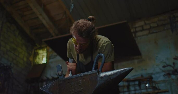 smith is using chisel for decorating forged item in workshop, work on anvil, 4K, Prores