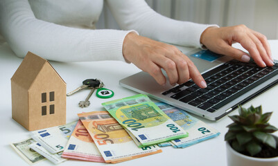 Woman's hands typing on laptop, banknotes of euro and house layout on white background. Economy, insurance and mortgage concept. - obrazy, fototapety, plakaty
