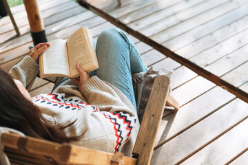 Brunette woman in nordic sweater reading book and relaxing in glamping in nature